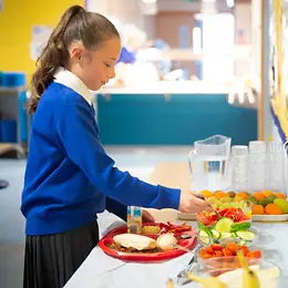 School girl adding vegetable to plate