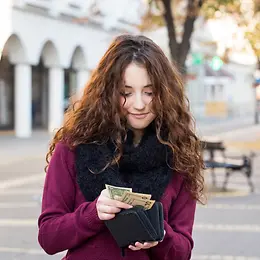 A young woman in an urban environment looks into her purse and counts the money.