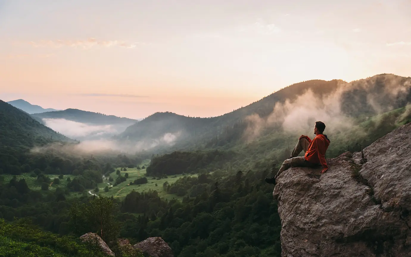 Young man sitting on rocky stone and enjoying view