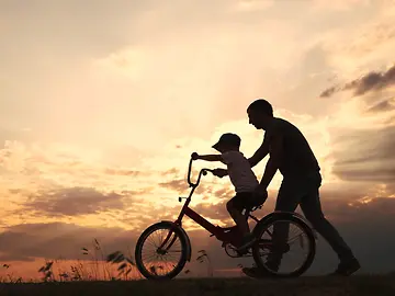 Parent helps child riding a bike